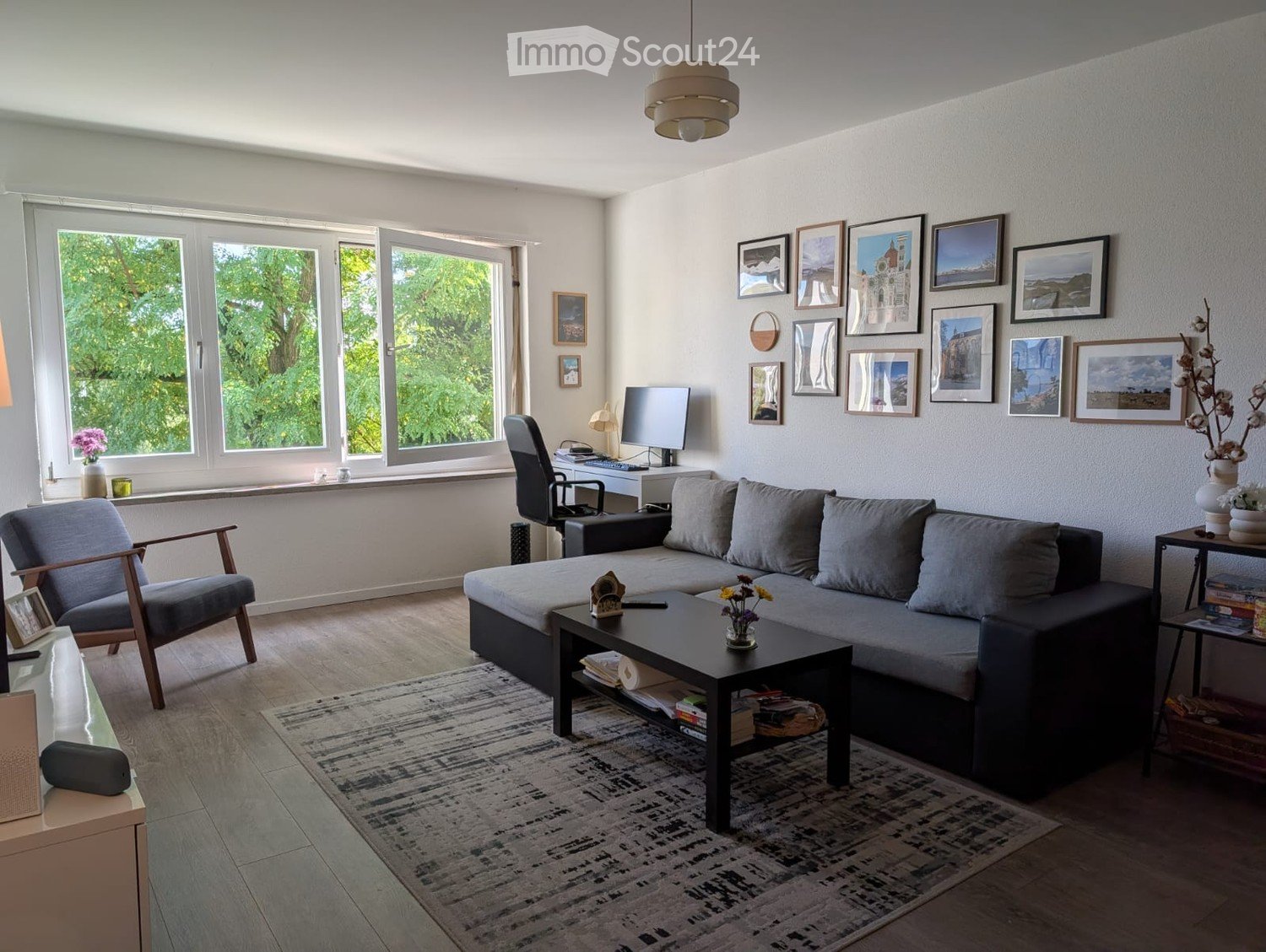 Modern living room with large windows, grey sectional sofa, coffee table, armchair, and decorative wall art.