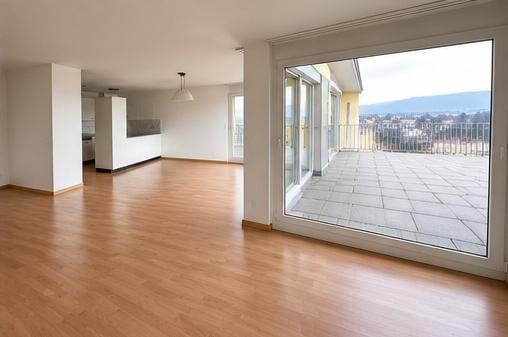 Bright, unfurnished living space with wooden flooring, large sliding glass doors leading to a tiled balcony, and a view of the city and mountains.