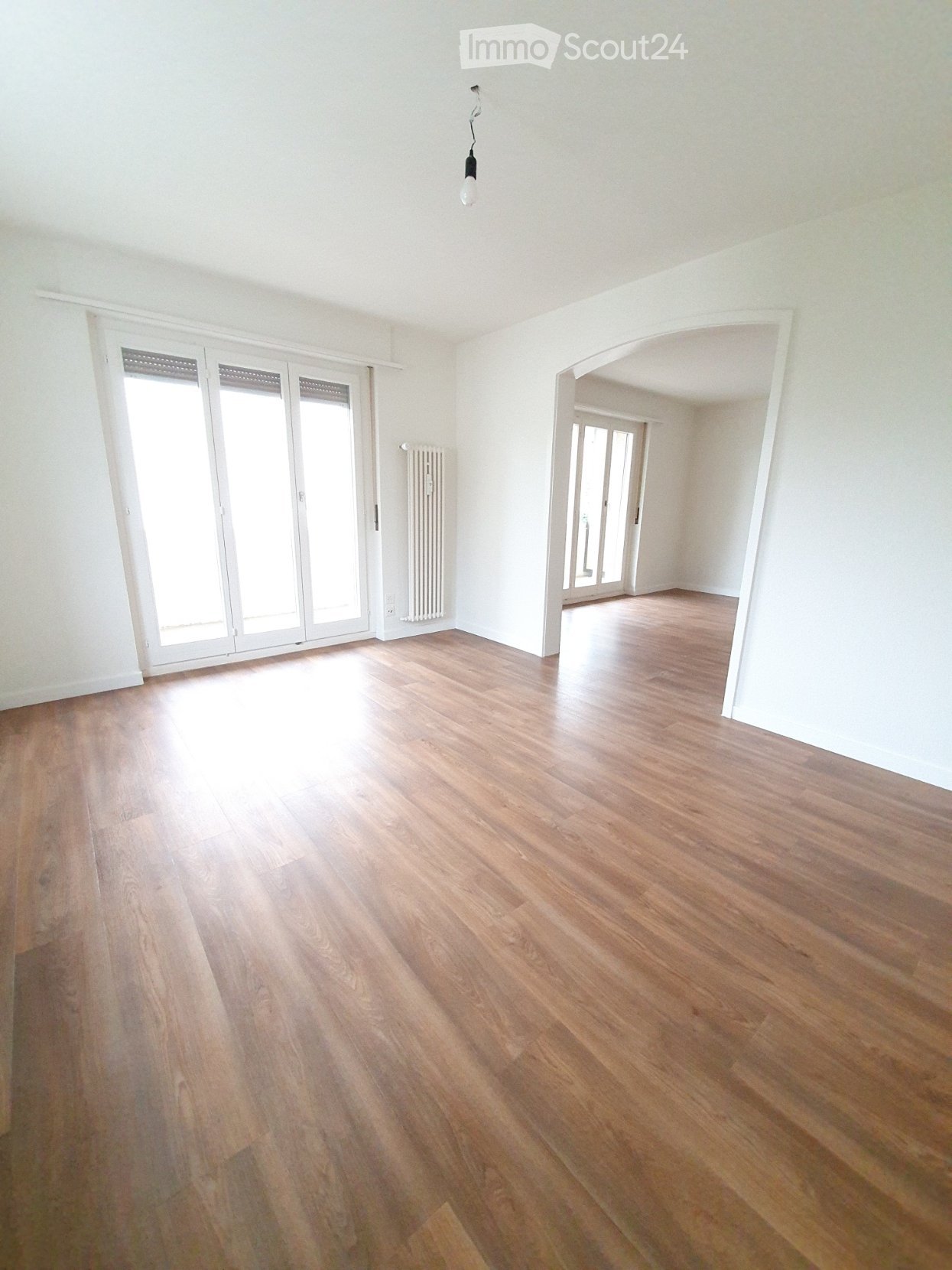 Empty room with wooden flooring, white walls, large sliding glass doors, and a visible radiator. No furniture or equipment present.