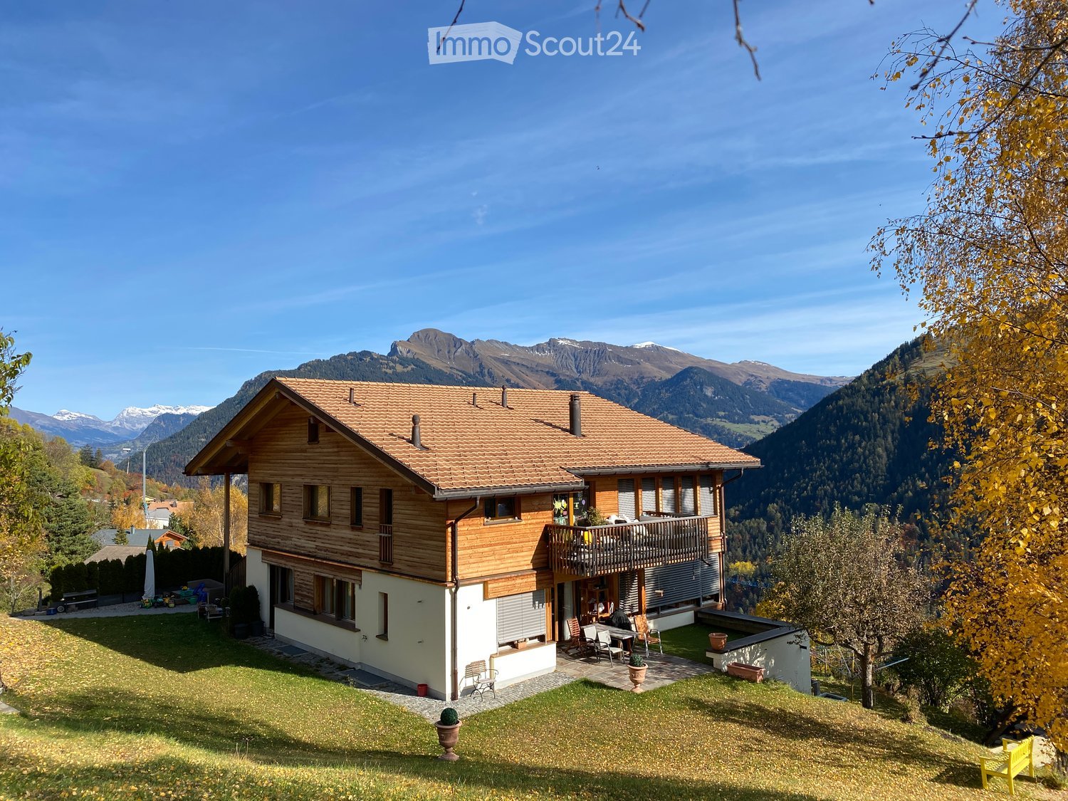 Two-story wooden house with a tiled roof, large windows, and a balcony overlooking a scenic mountain view.