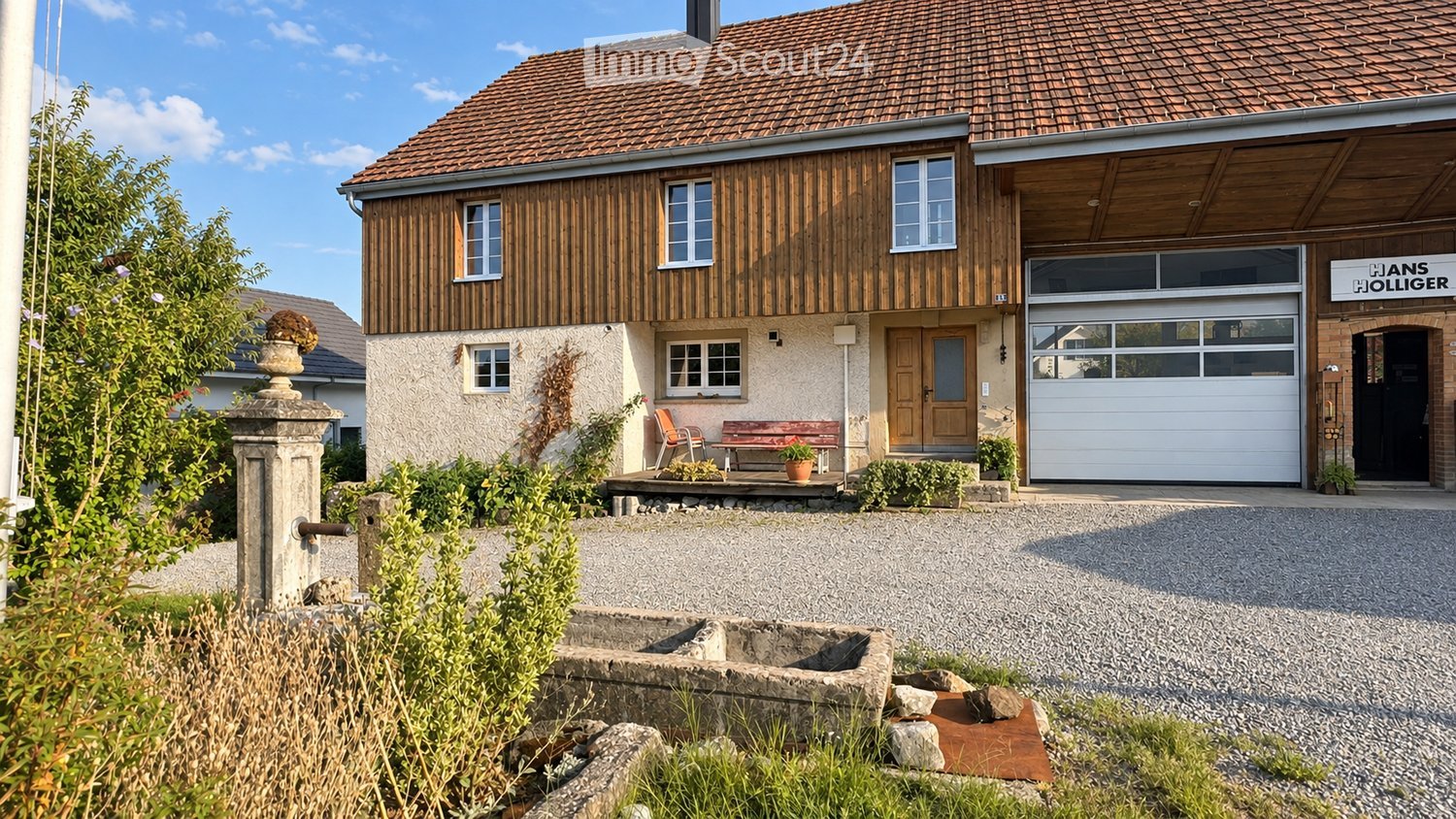 Two-story house with a tiled roof, wooden facade, garage, and small porch with seating area.