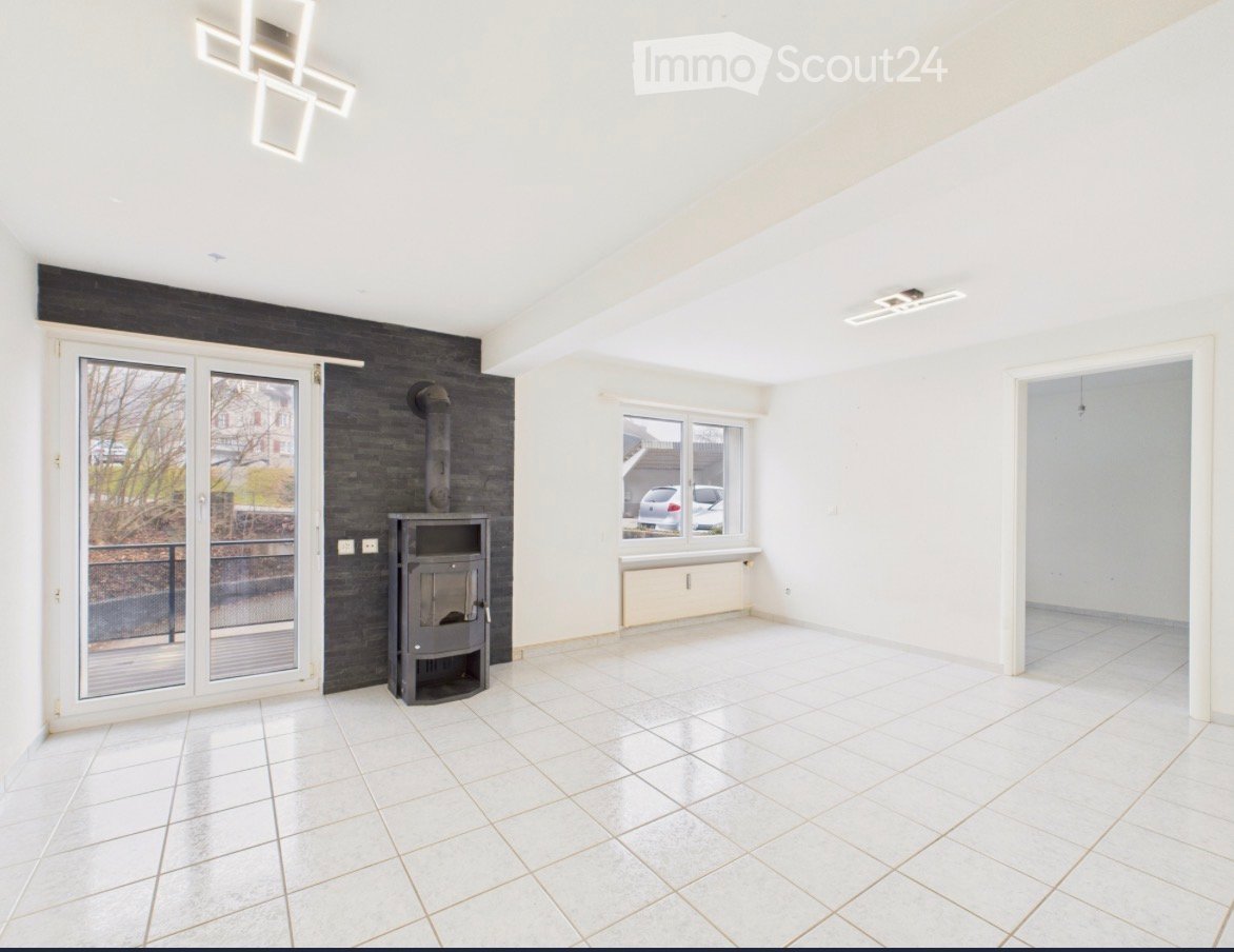 Empty room with white tiled flooring, white walls, large windows, and a black wood-burning stove.