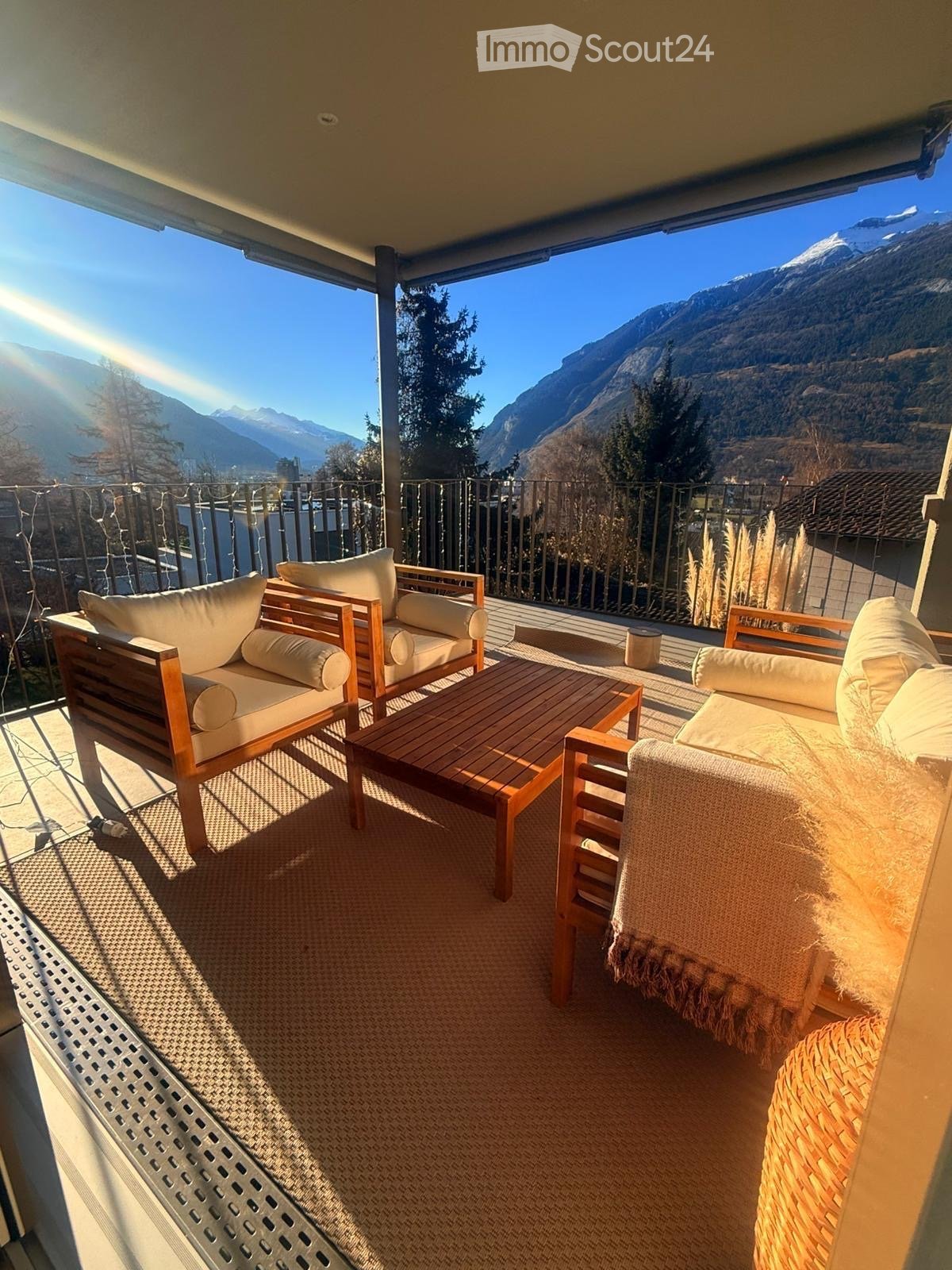 Balcony with wooden furniture, including a sofa, table, and chairs, overlooking a mountain view.