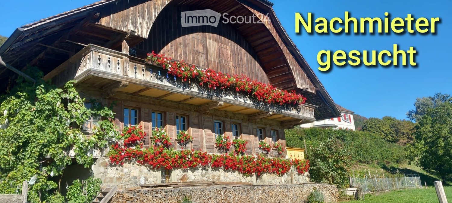 Traditional wooden house with stone base, balconies adorned with red flowers, and lush greenery climbing the walls.
