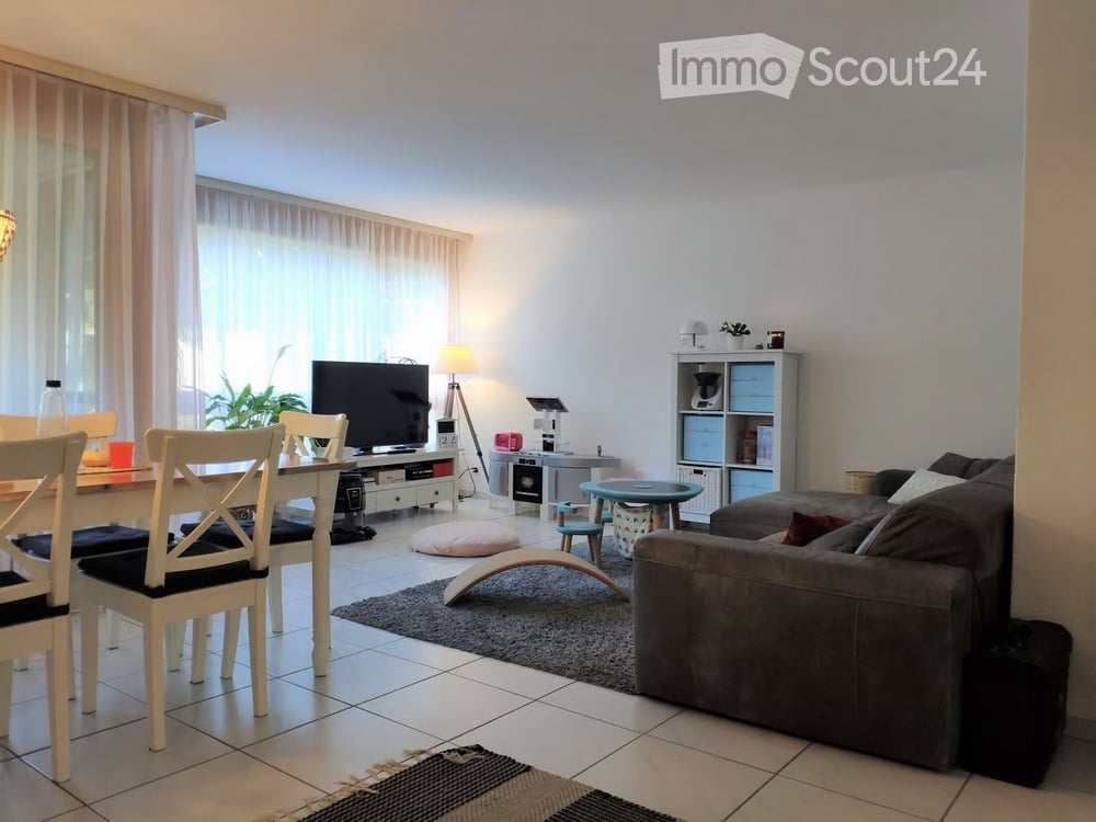 A modern living room with a grey sofa, coffee table, dining table with chairs, television, floor lamp, small round table, and decorative items.