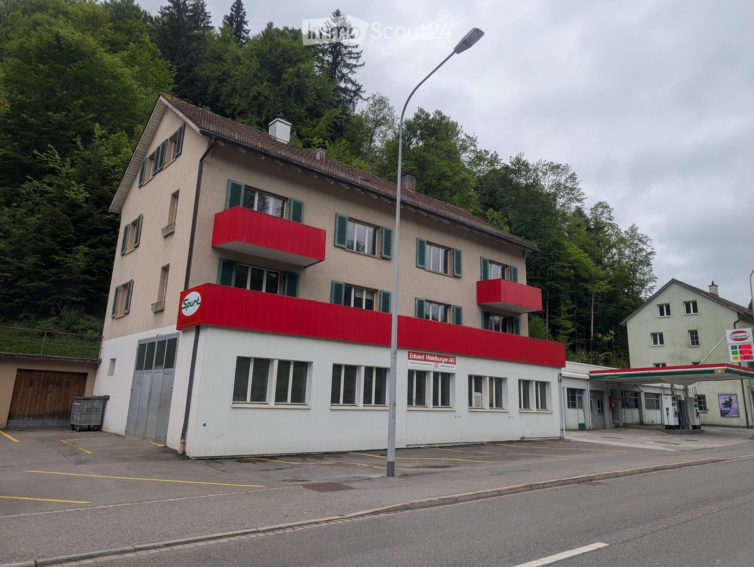 Two-story building with red awnings, multiple windows, and a gas station attached.
