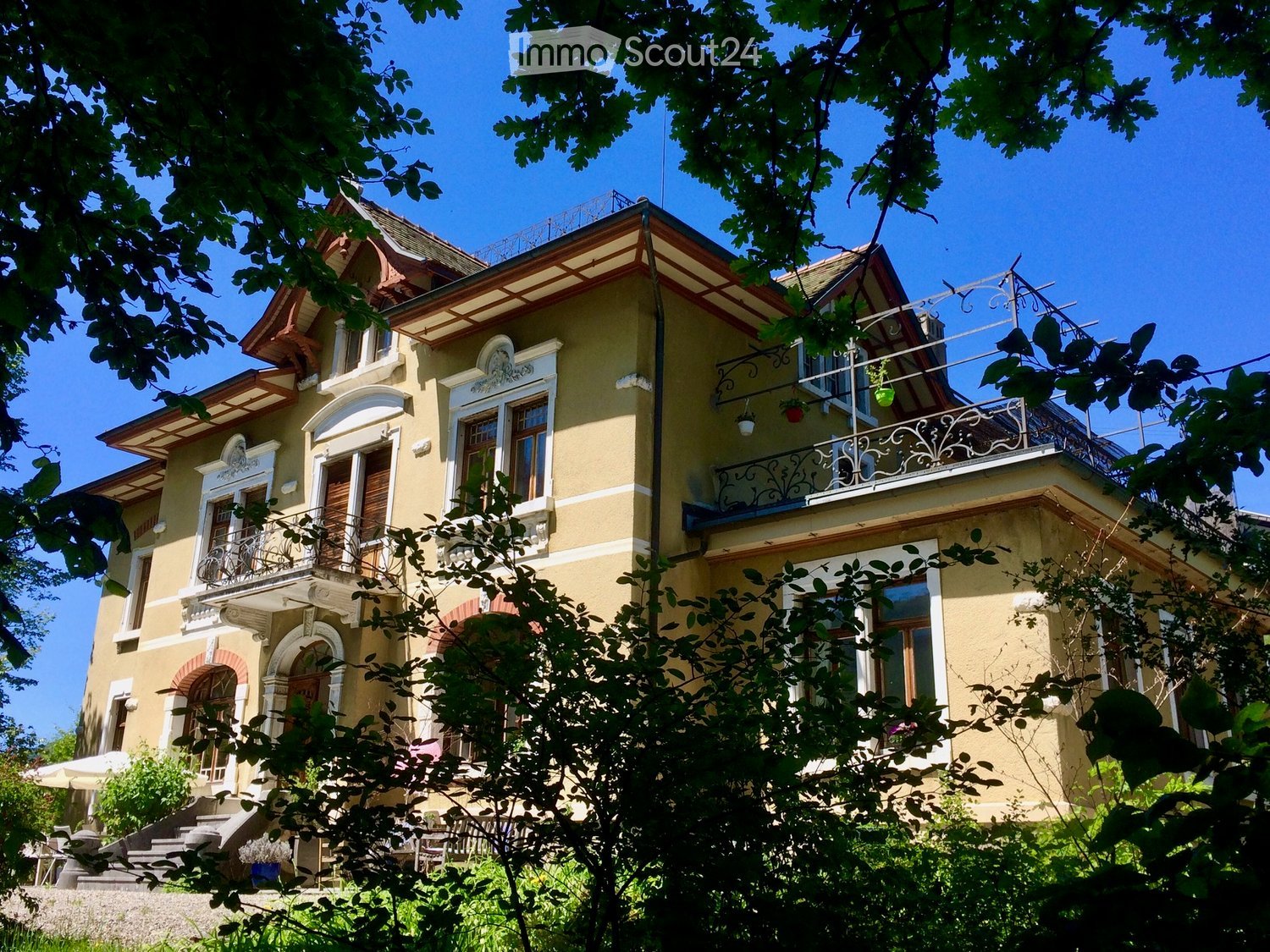 A two-story yellow house with white trim, multiple balconies, ornate railings, and decorative architectural details.