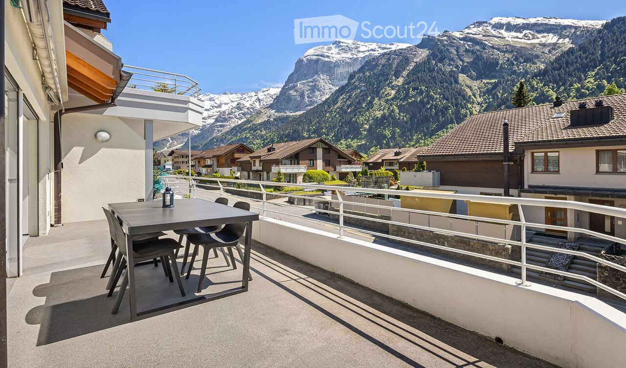 Balcony with a table and chairs, overlooking a scenic mountain view and village.