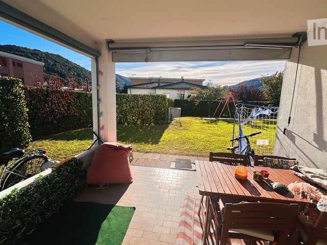 Balcony with outdoor dining table and chairs, overlooking a green garden and distant mountains.