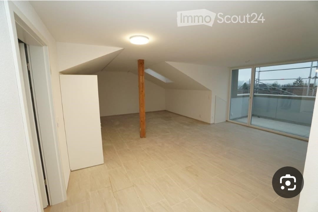 Empty attic room with wooden floor, white walls, large skylight, and sliding glass door leading to a balcony.