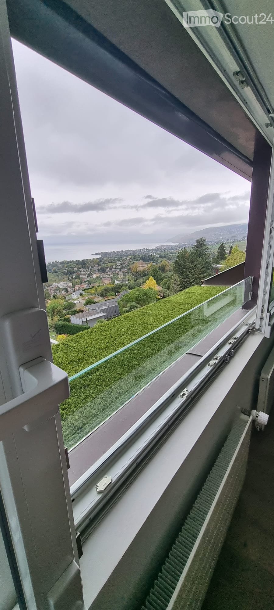 View from a balcony showing a scenic landscape with a lake, town, and hills in the background.