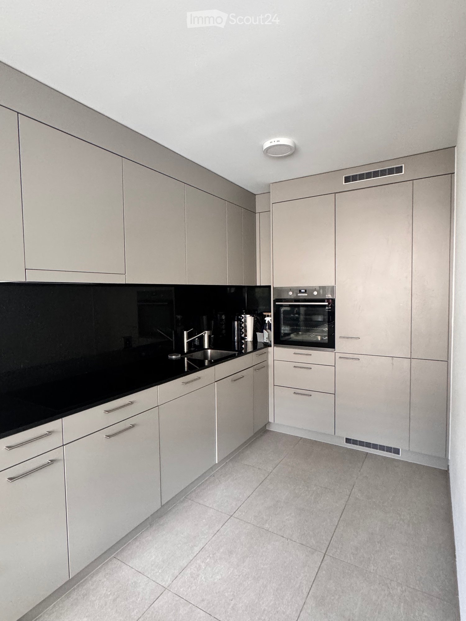 Modern kitchen with light grey cabinets, black countertop, stainless steel sink, and built-in oven.
