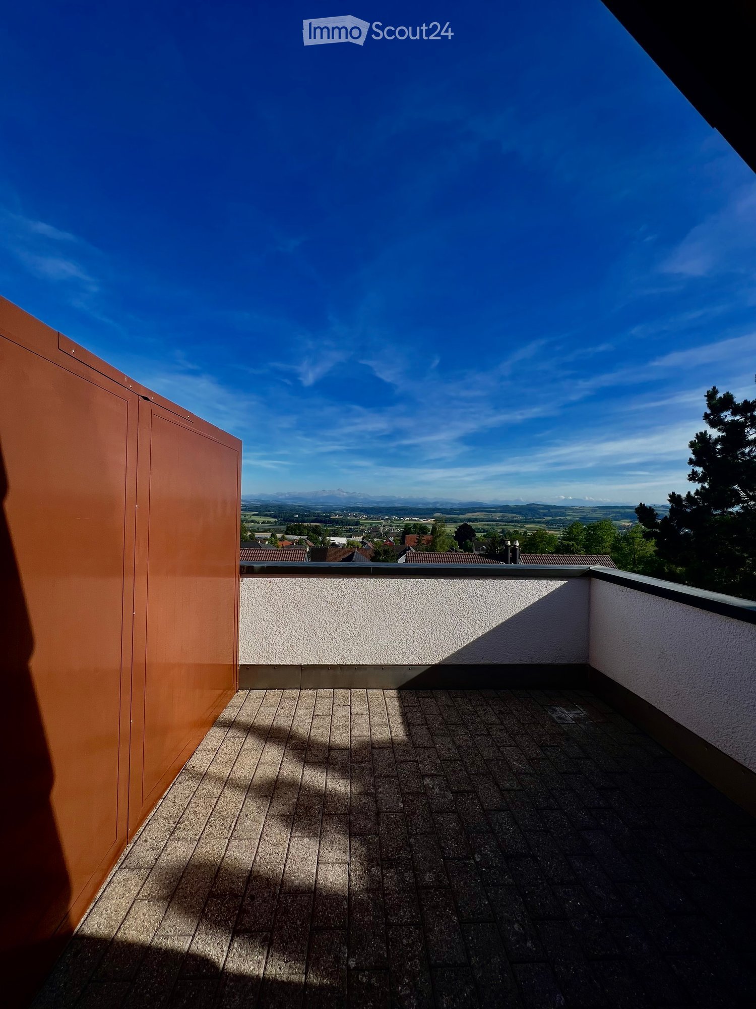 Balcony with tiled floor, white walls, and a scenic view of a valley and mountains under a clear blue sky.