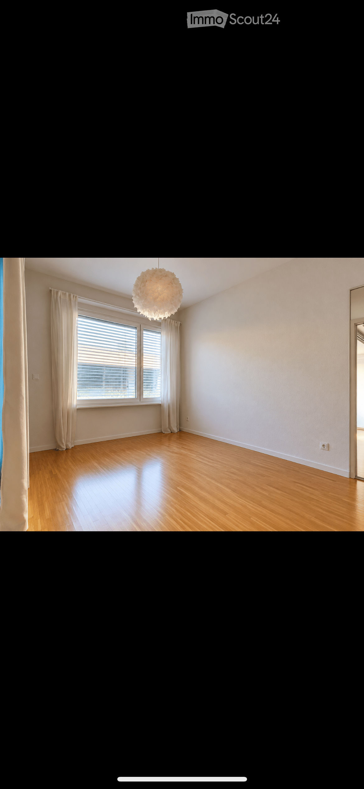 Empty room with wooden flooring, large window with blinds, and a hanging light fixture.
