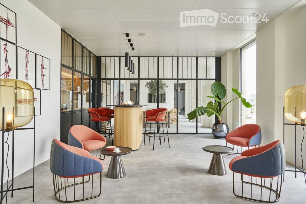 Modern lounge area with contemporary furniture including chairs, tables, a bar counter, and decorative lamps. Large windows and a plant add to the ambiance.