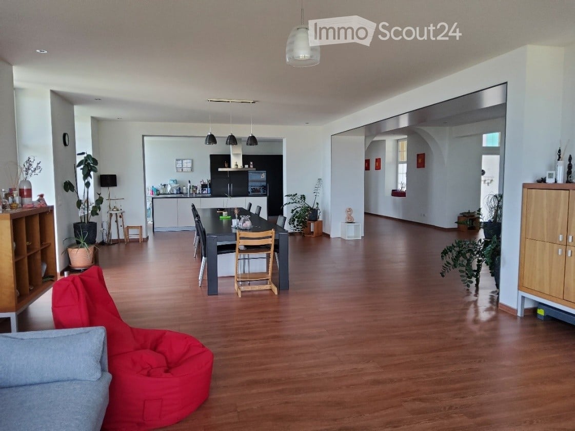 Open-plan living and dining area with wooden flooring, a red bean bag chair, a dining table with chairs, and a modern kitchen in the background.