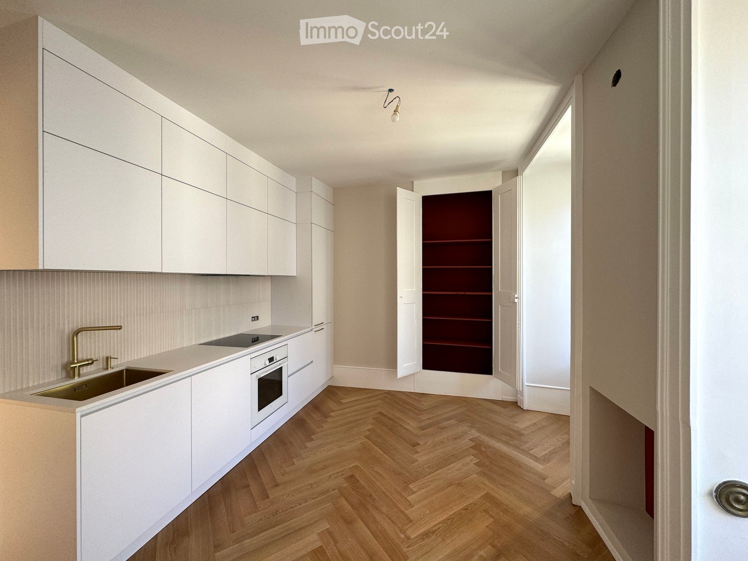 Modern kitchen with white cabinets, wooden herringbone flooring, and a stainless steel sink and oven.
