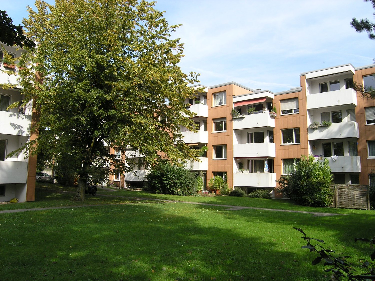 multiple story apartment buildings, balconies, potted plants, landscaped front lawn, grassy area, tree