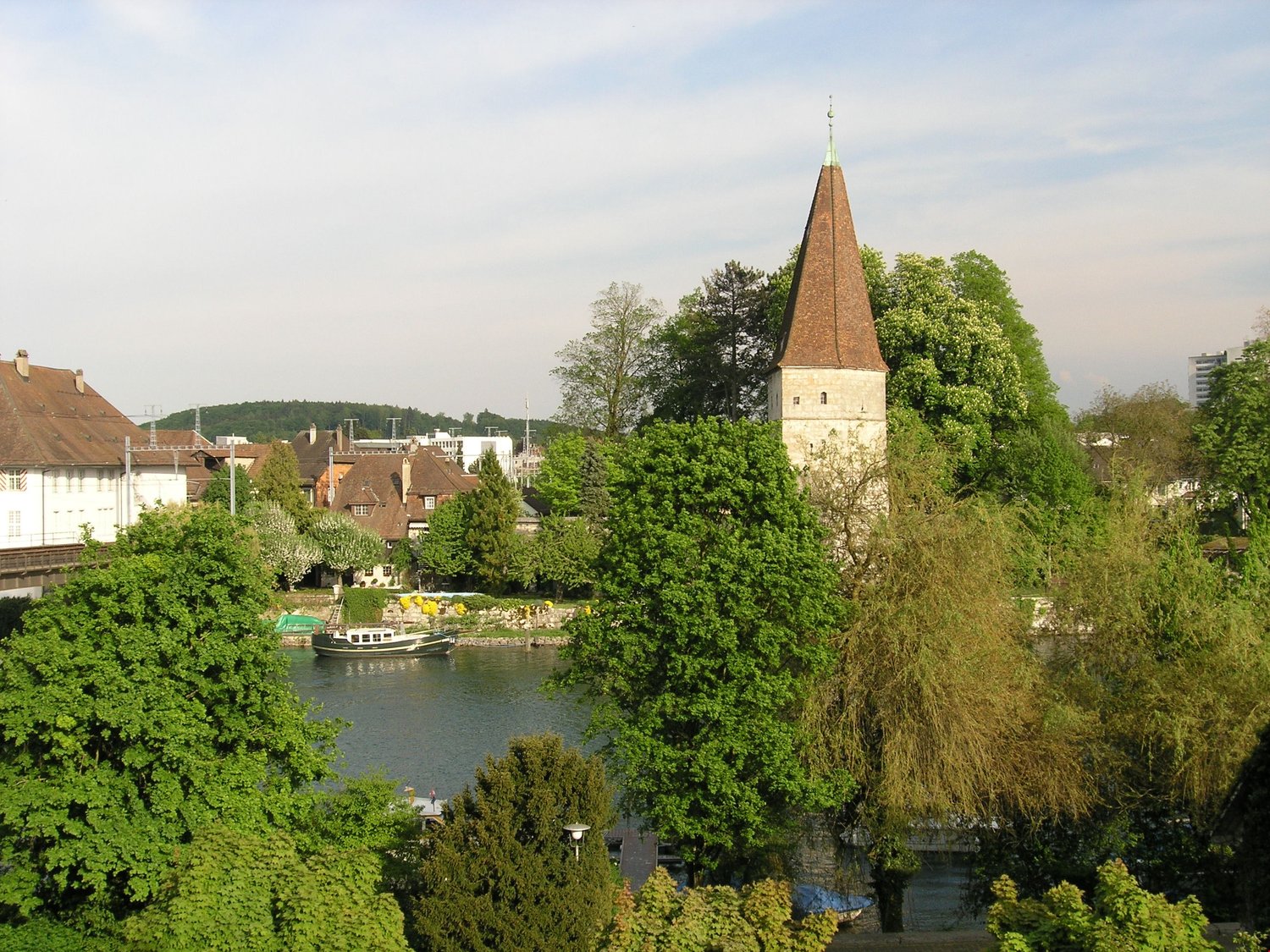 river, old town buildings, church tower, trees, boats