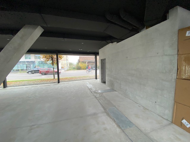 concrete wall, ceiling with beams, open parking area, person riding a bike on road
