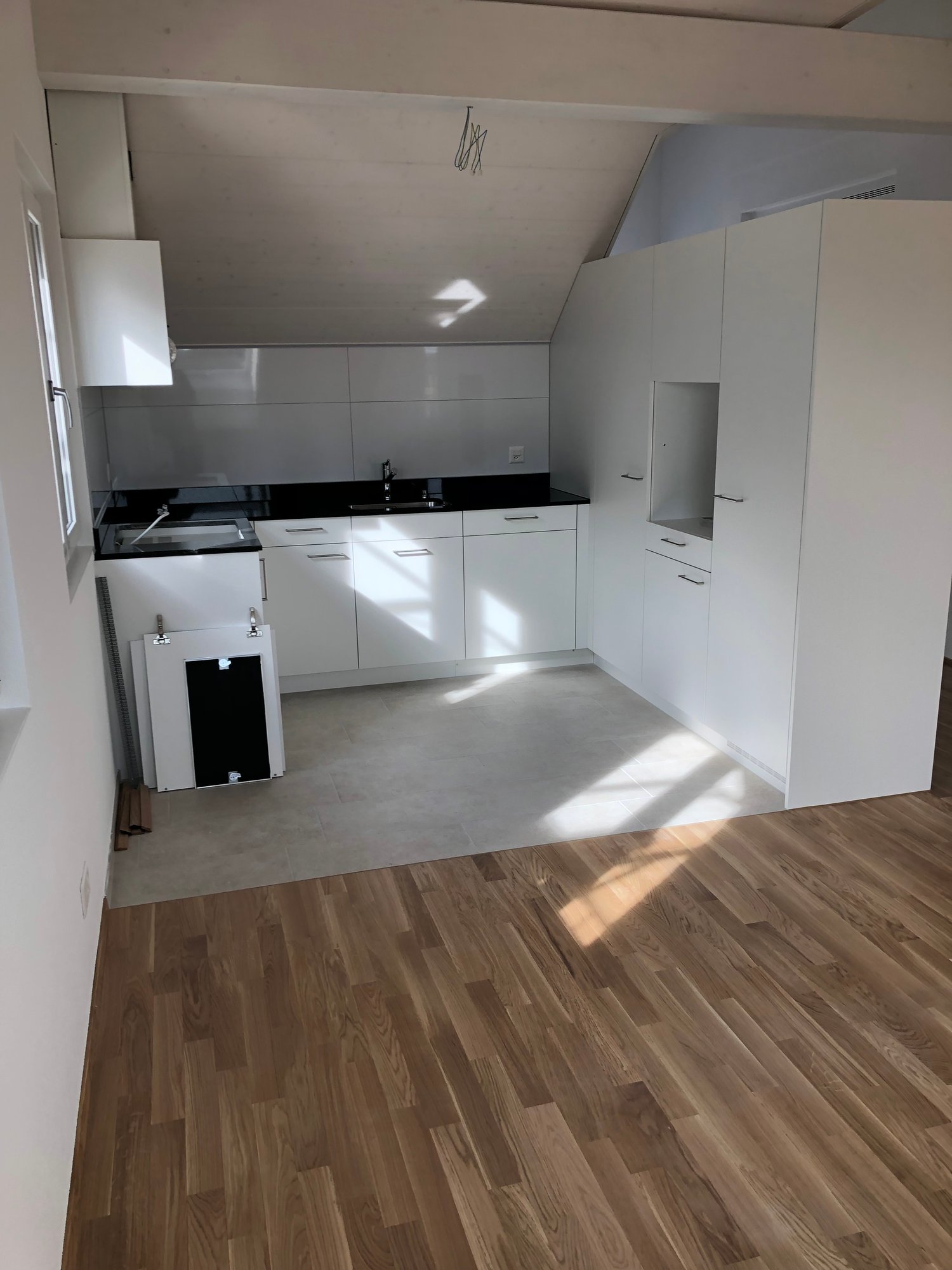 Minimalist kitchen with wooden floors, white cabinets, black countertops, and modern fixtures