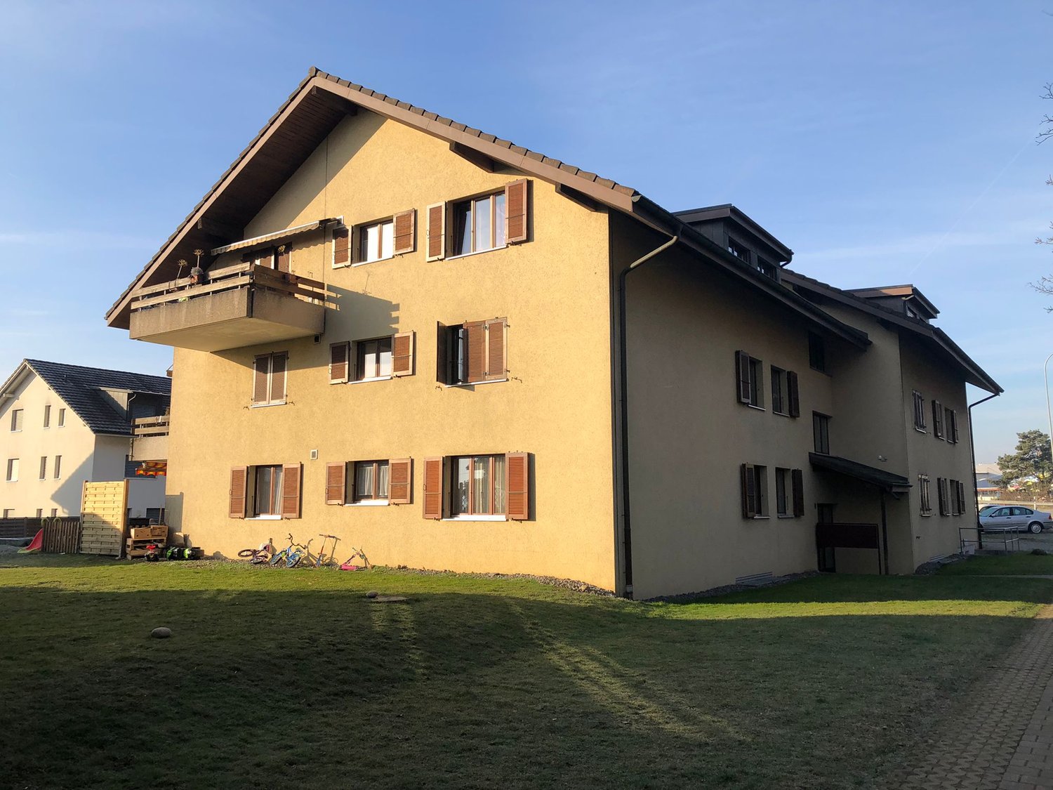 2 story house, beige paint, brown shutters, balcony, green lawn, parking space in front