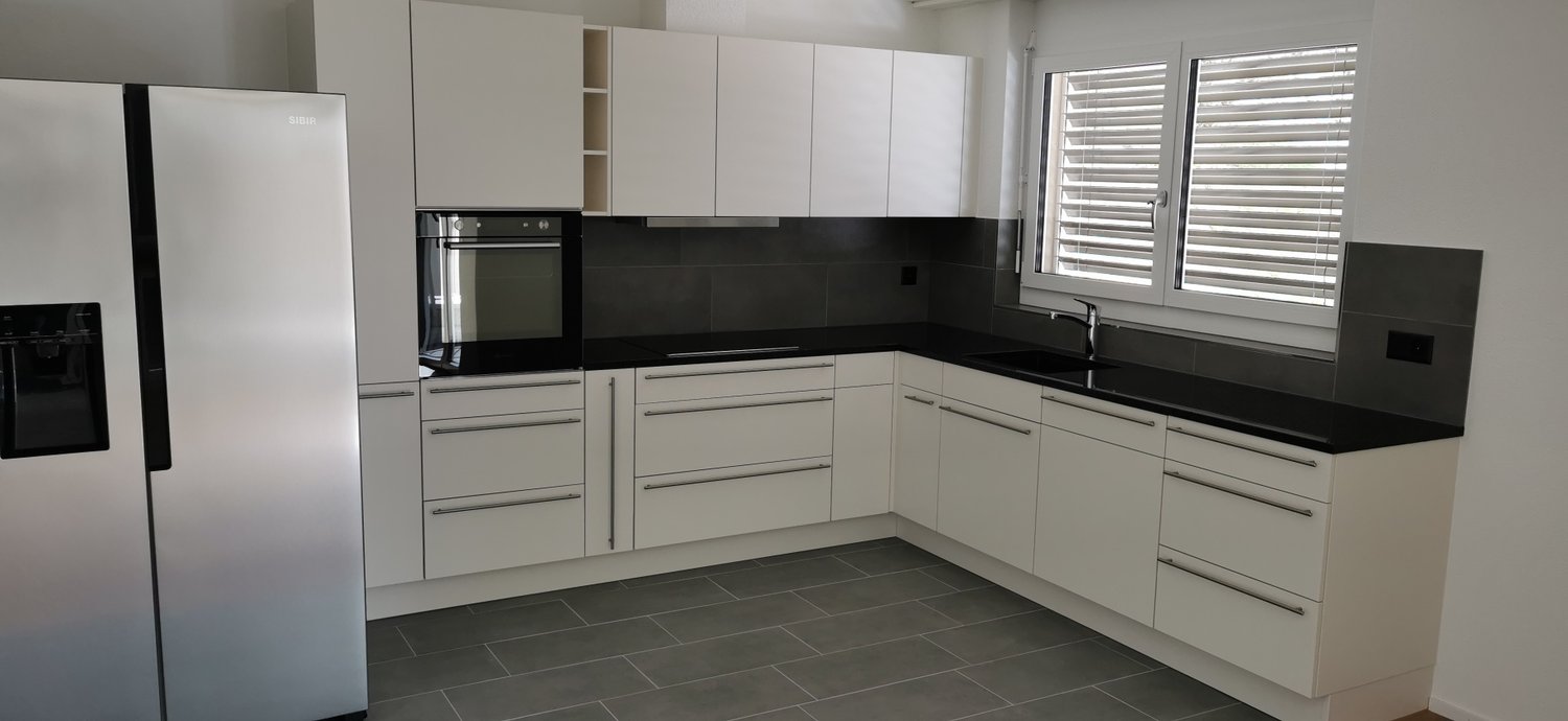 modern design, white cabinets, black countertops, stainless steel refrigerator, integrated oven, faucet, windows with blinds, tiled floor