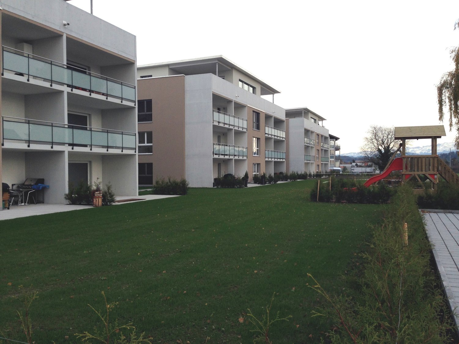 4 story residential building with balconies, well maintained lawn, children's playground