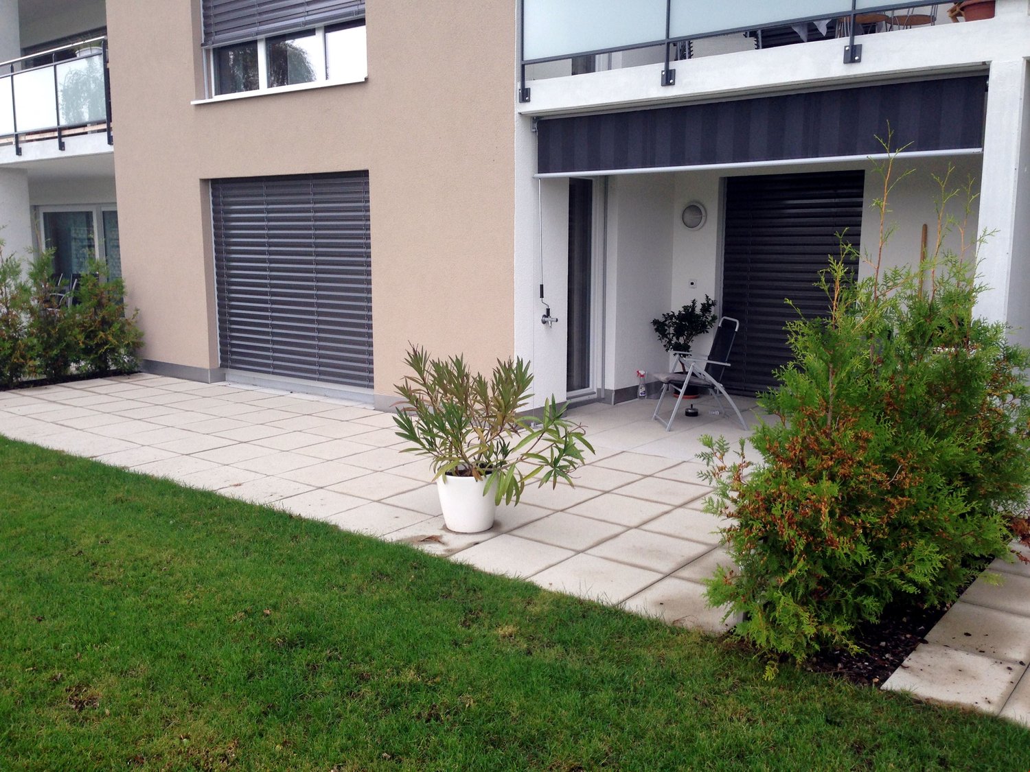 House exterior with tiled walkway, 2 garages, small lawn, balcony, and plants