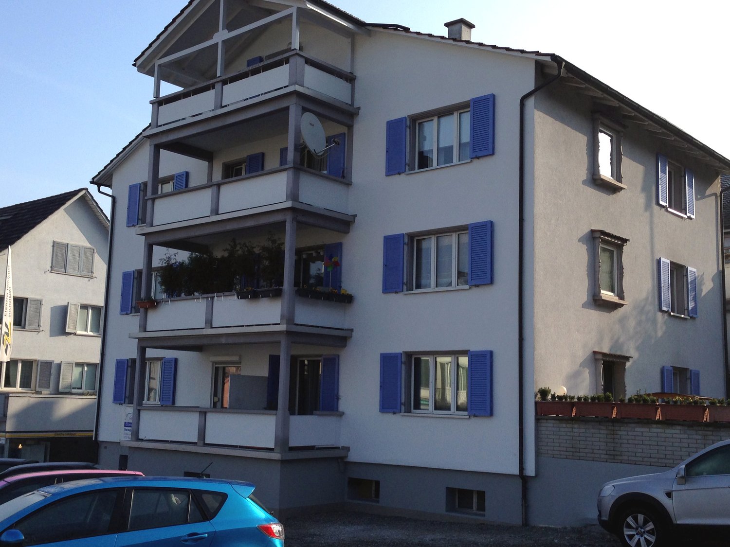Four story building, white exterior, blue shutters, balconies, chimney, parking in front