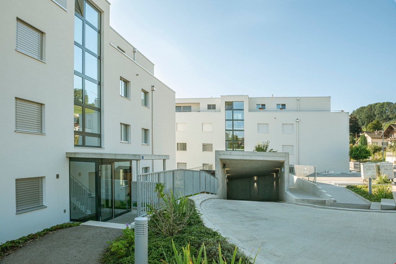 Multi-story apartment building with a garage entrance, glass windows, and landscaping around the entrance.