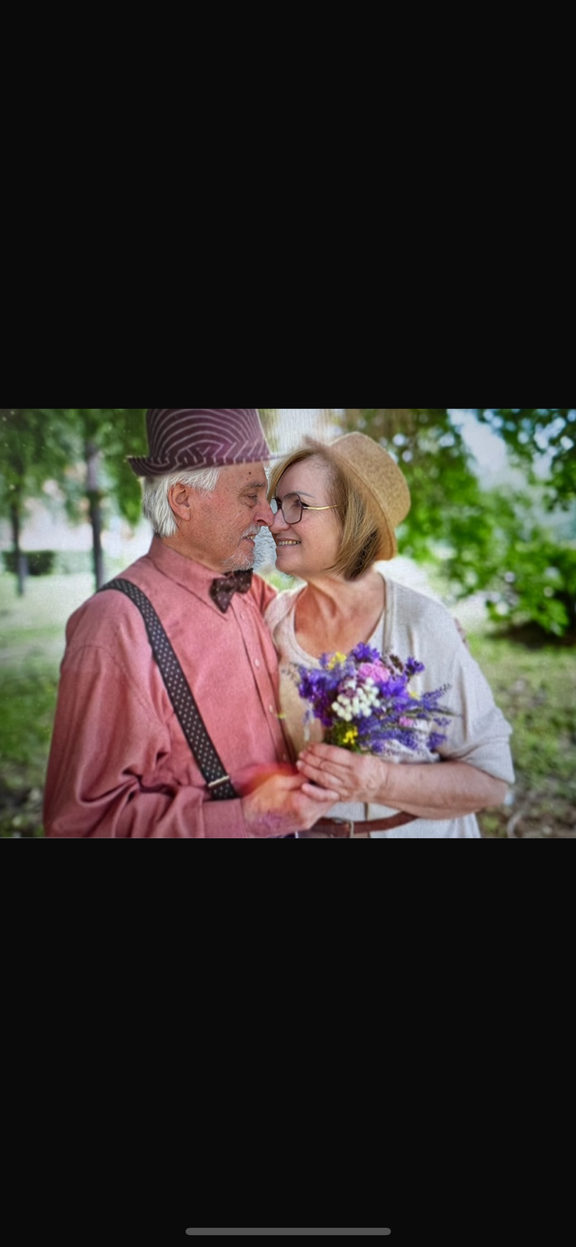 An elderly couple holding each other, a man in suspenders and hat, a woman in a hat holding a bouquet of flowers, they are in a park surrounded by green grass and trees