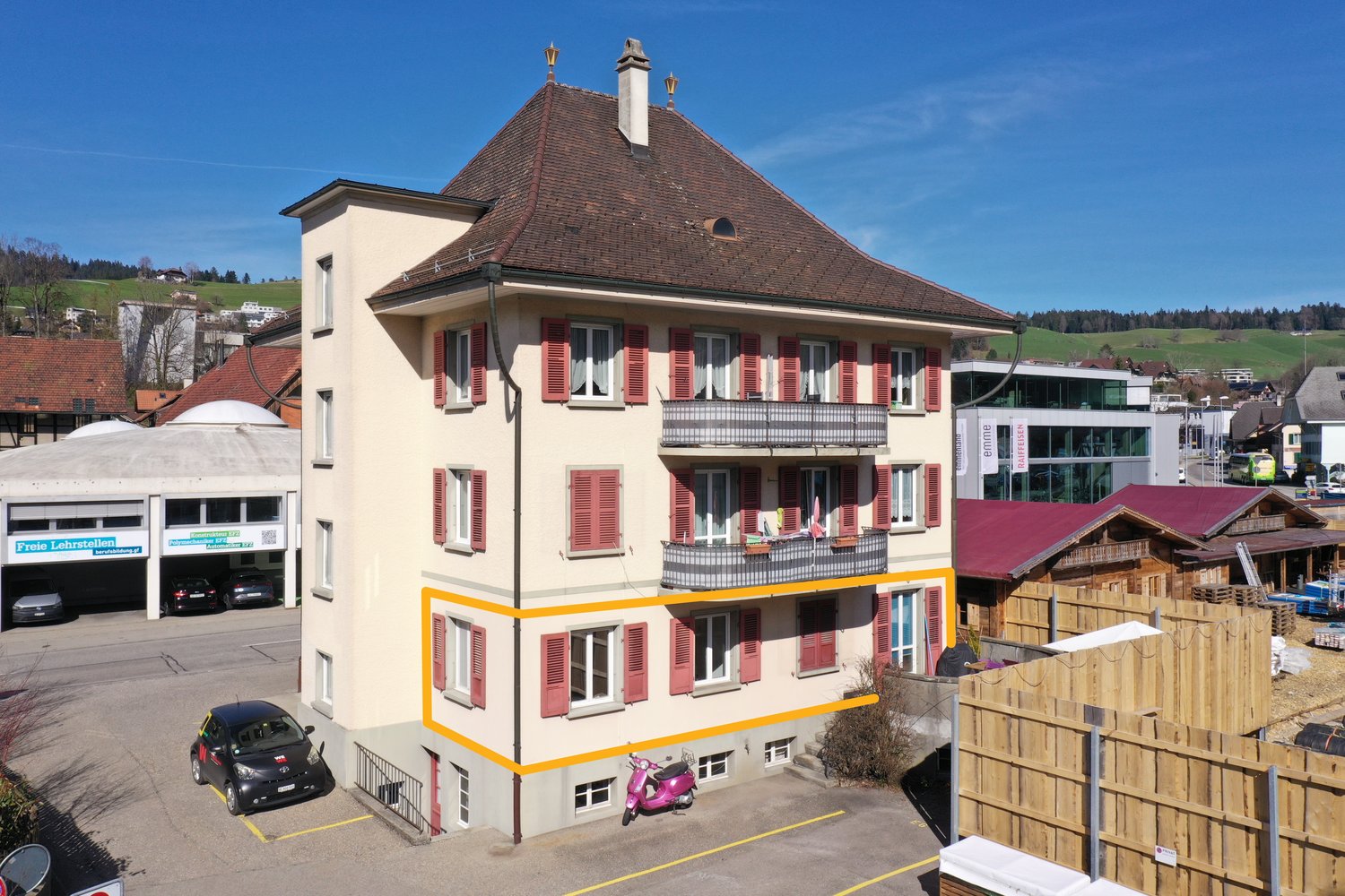 4-story building, beige exterior, red roof, multiple balconies, located in a parking area