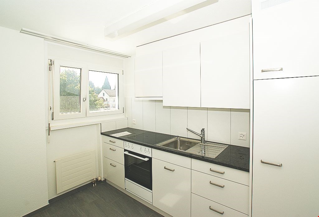 Modern, white kitchen with tiled floor and countertops, equipped with oven, sink, faucet, and dishwasher