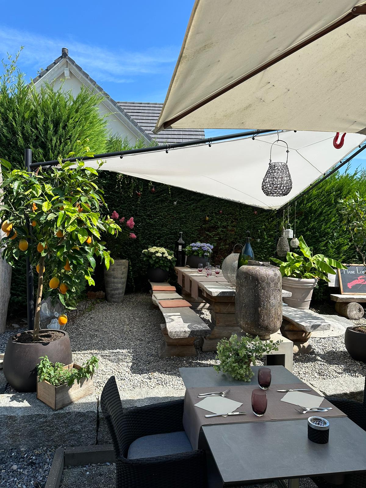 Outdoor dining area with a large table, stone benches, umbrella, plants, and decorative elements