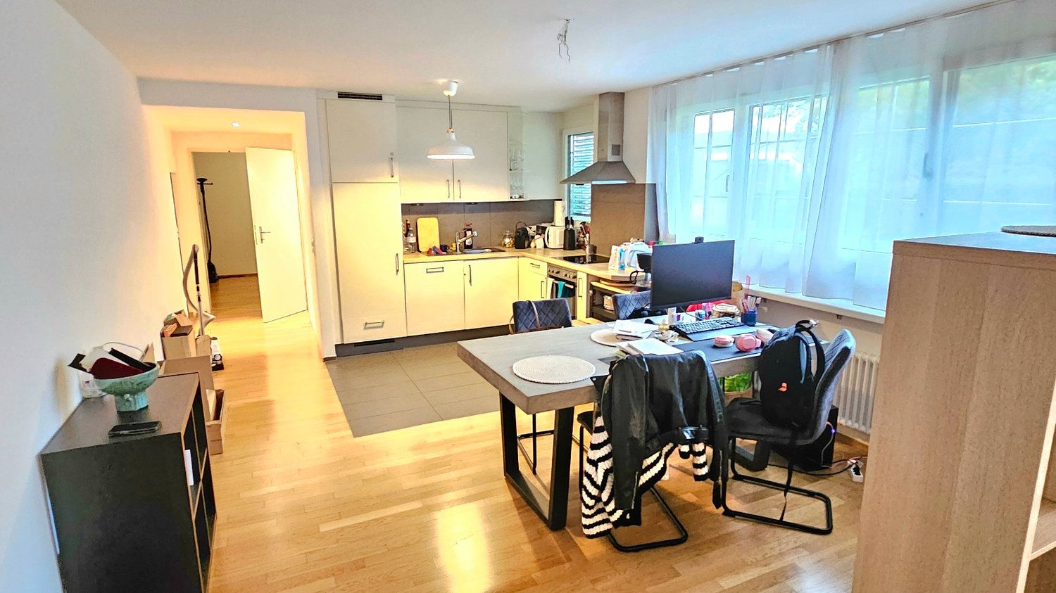 dining room with large windows and modern kitchen area, wooden floor, desk with chairs, lamps