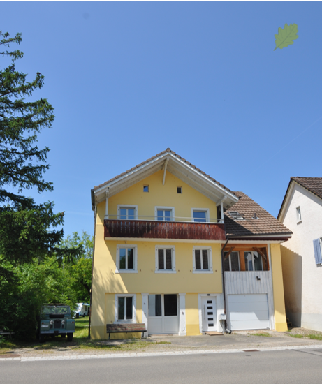 2 story house, yellow exterior, brown roof, white windows, bench, garage