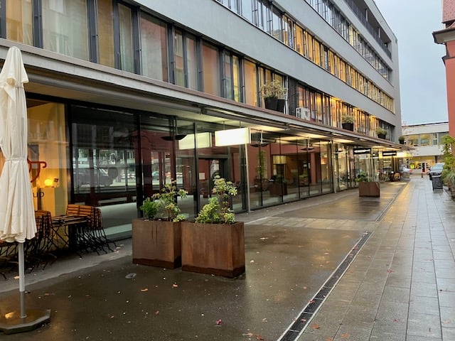 modern office building with glass walls, metal roof, patio with table and chairs, outdoor plants