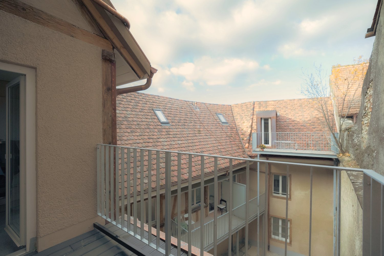 View of a building exterior with balconies, red roof, multiple floors, metal railings.