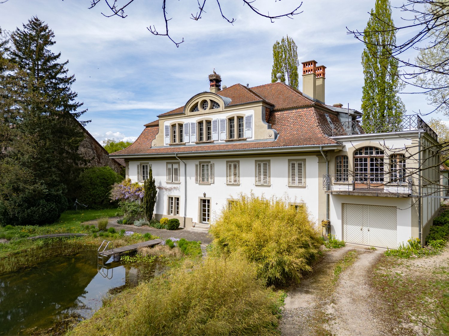 3 story house, white exterior, brown roof, garage, small pond, garden