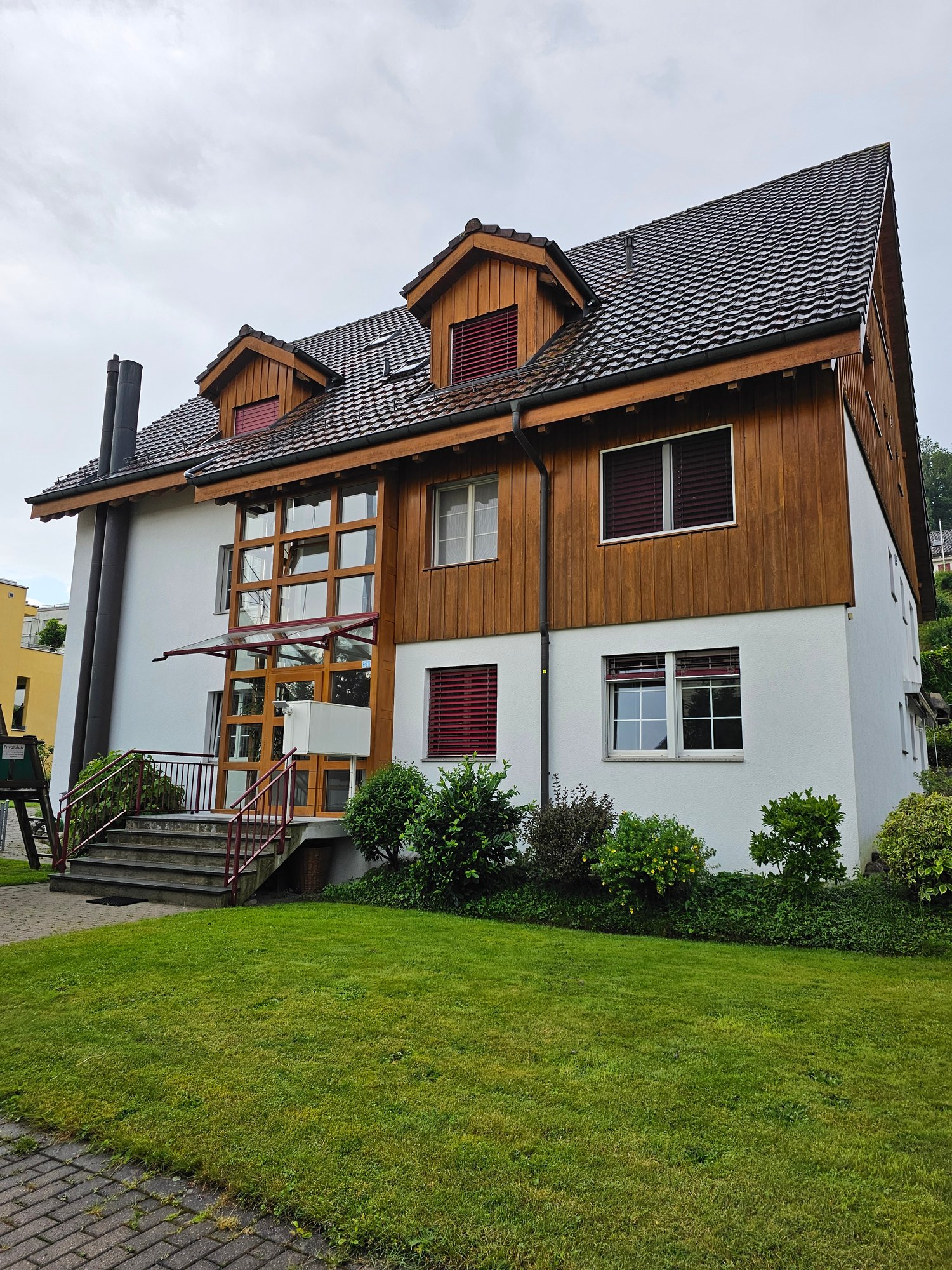 Detached house, wood and white brick, tiled roof, multiple windows, front stairs, landscaped front