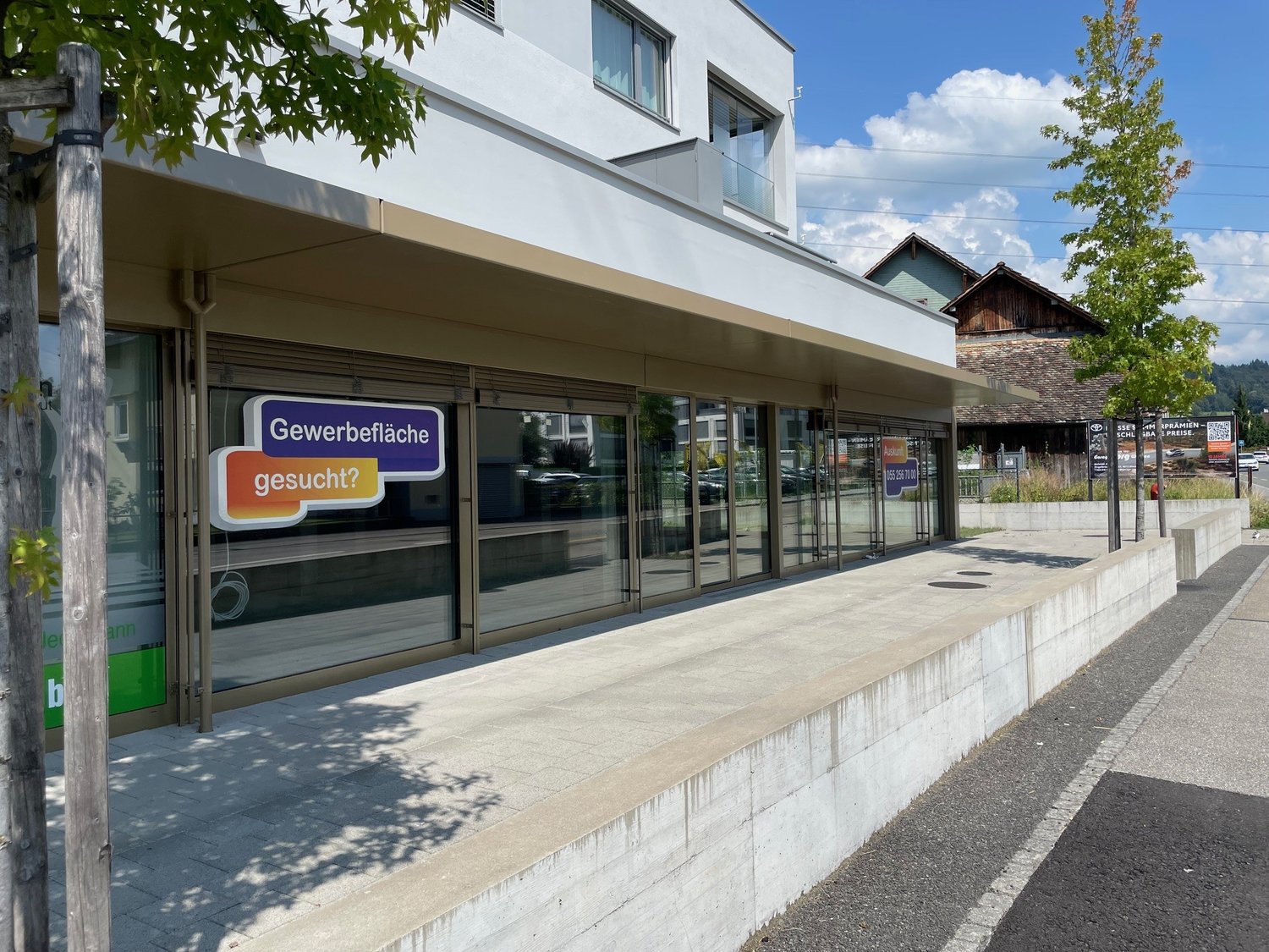 Commercial building with glass facade, sign reading 'Gewerbefläche gesucht?'