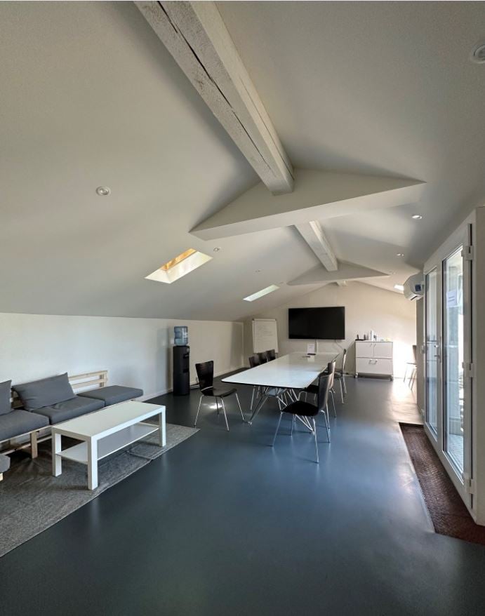 A well lit room with a table, couch, chairs, television and a water dispenser.