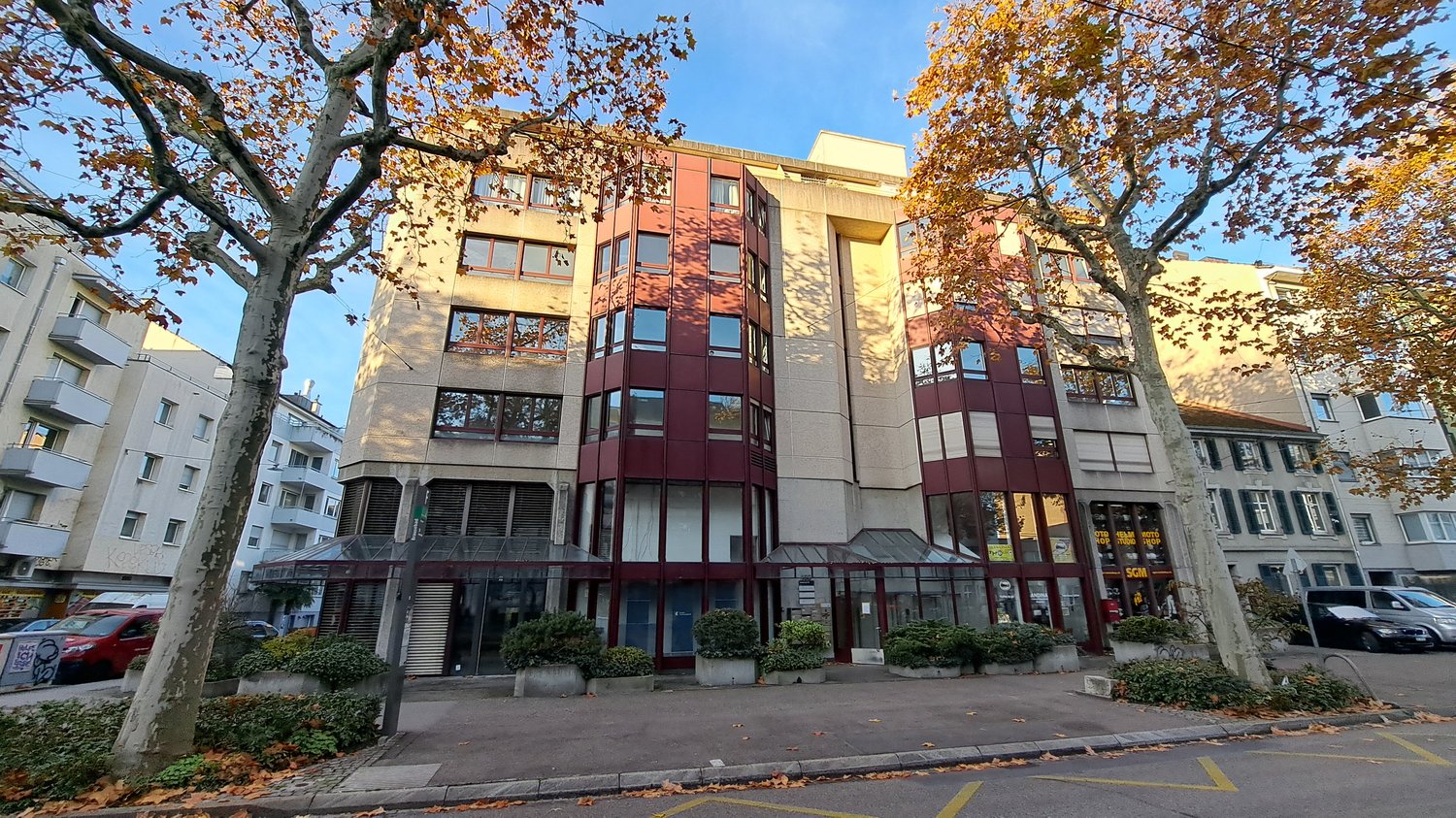 Office building, 6 floors, brick walls, glass windows, awning, raised ground floor, shrubs, parking area