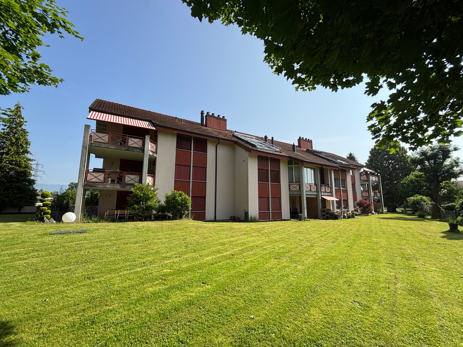 2-story apartment building with red and white exterior, balconies, surrounded by a well-maintained lawn and trees