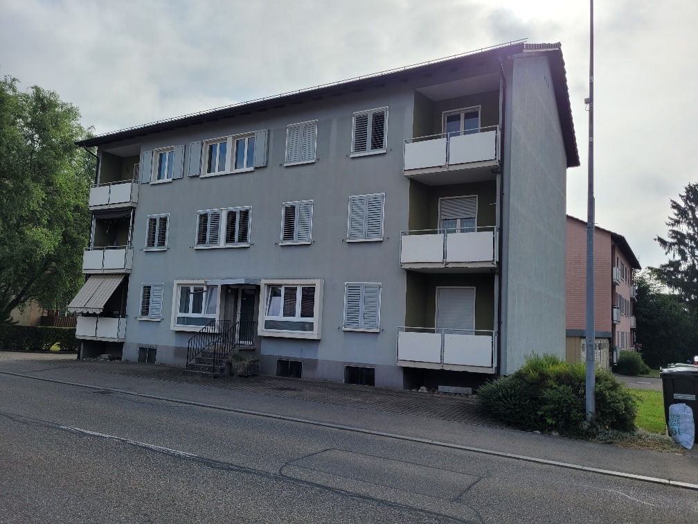 Apartment building with 3 floors, balconies, gray walls, white shutters, entrance on ground floor