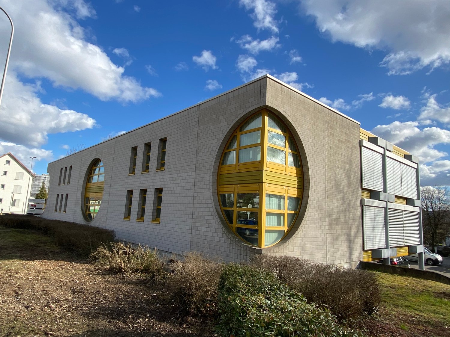 Modern building with a white brick facade, large yellow arched windows, and a circular window on the front.