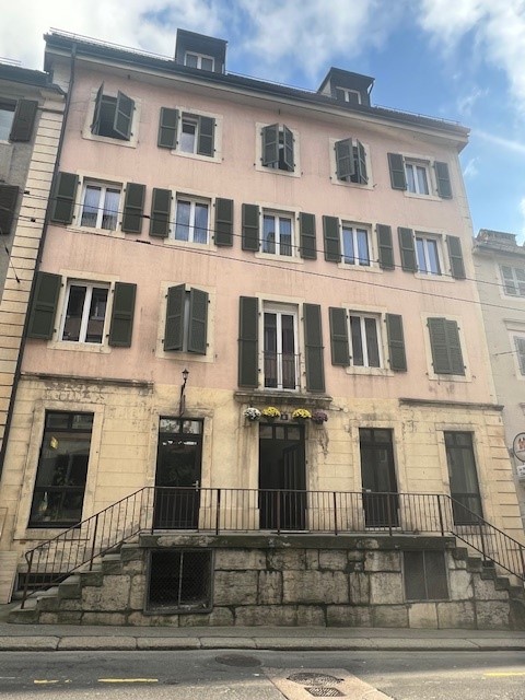 pink building, multiple windows, several floors, raised ground floor, black railings, flowers hanging from balconies, small shops