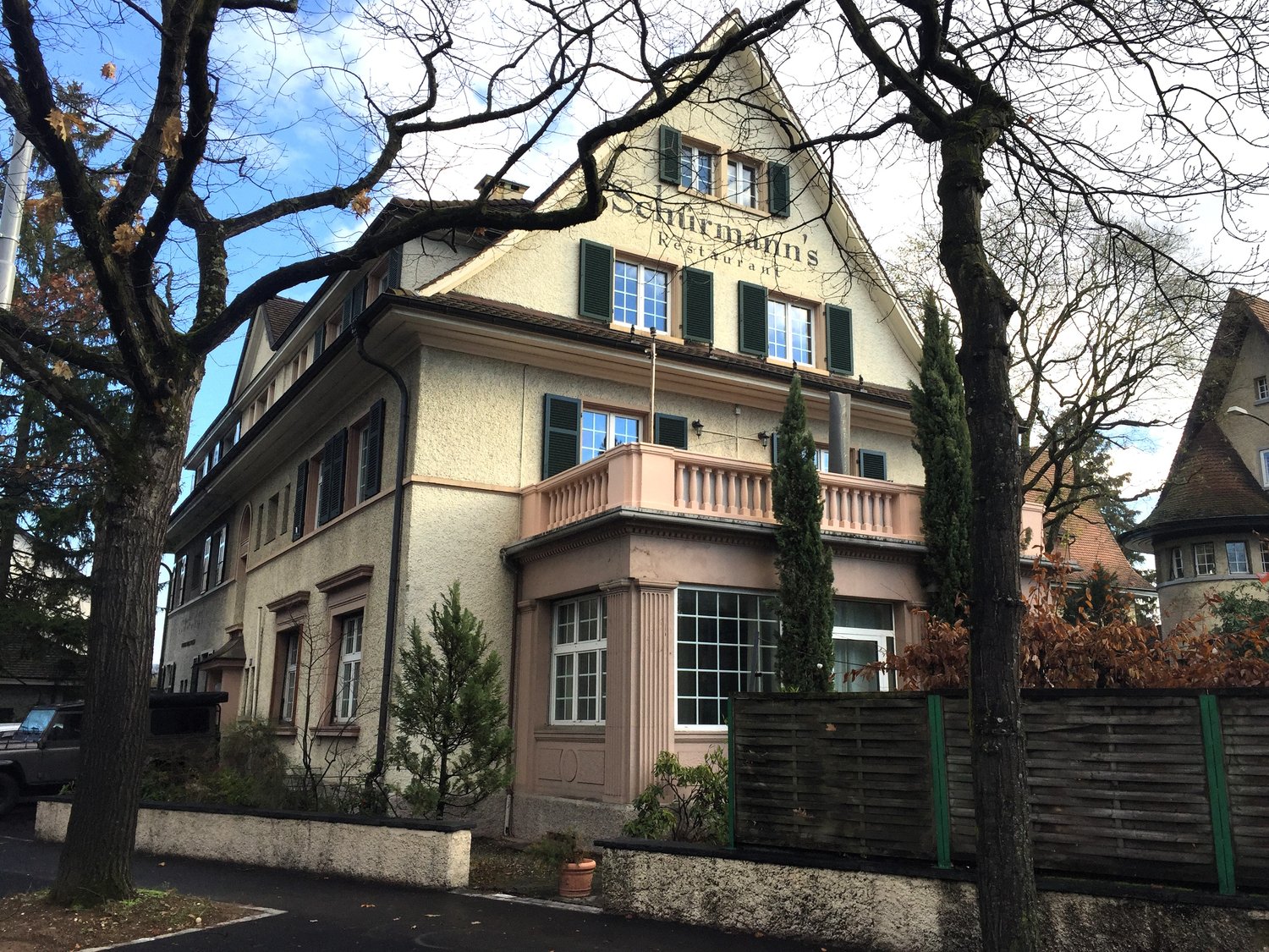 Building with multiple windows, brown roof, a balcony, with a sign 'Schurrmann's Restaurant' above it.