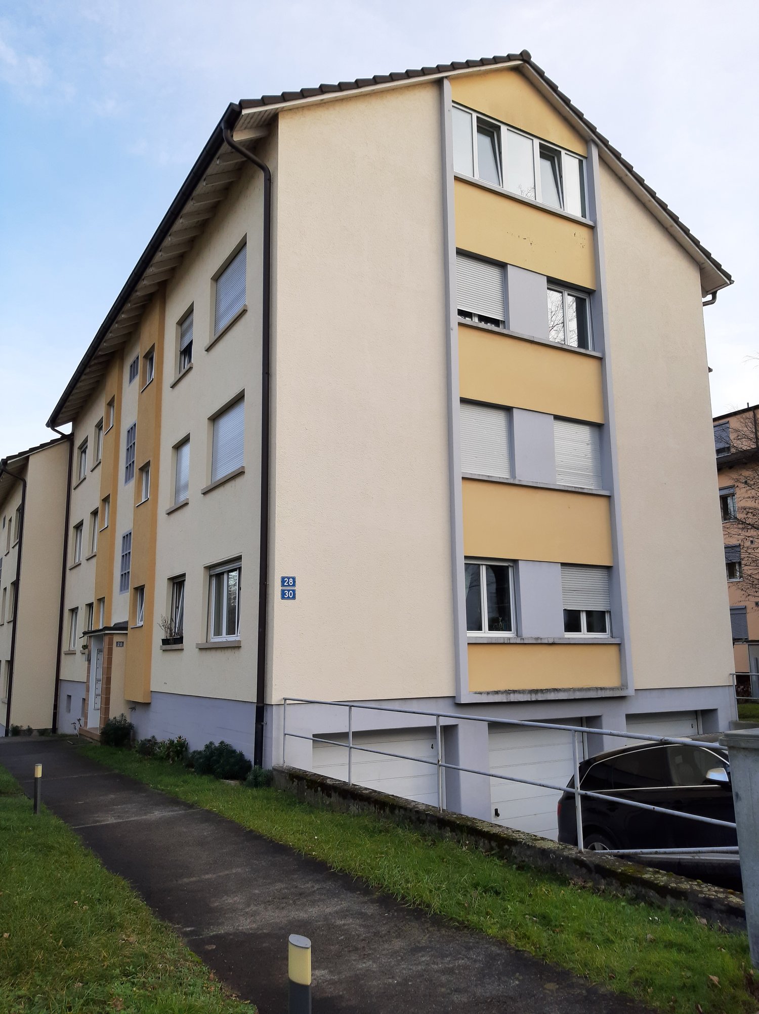 4 story residential building, beige and yellow exterior, large windows, balconies, garages, path